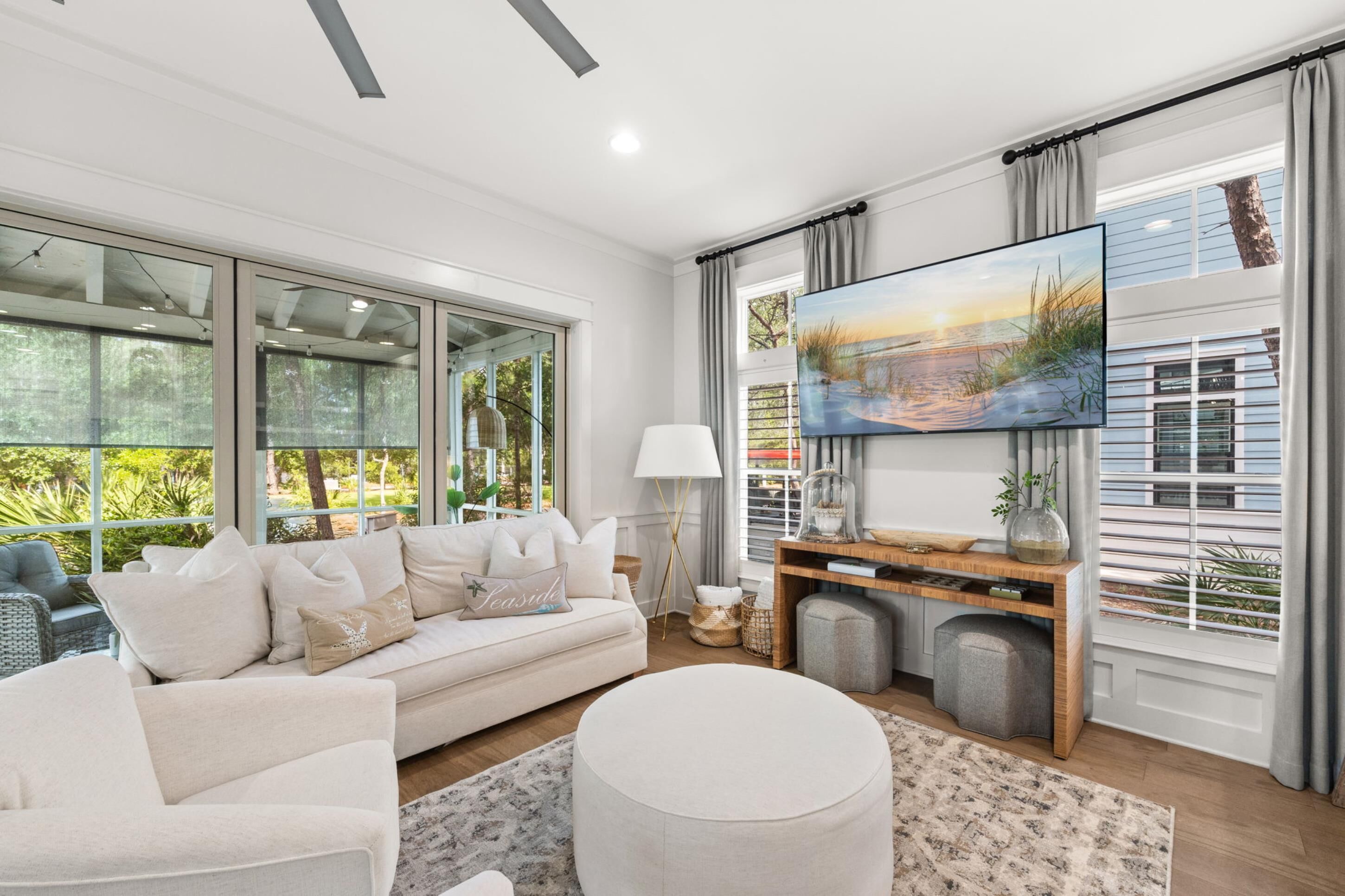 A modern living room with a large window, a sofa, a coffee table, and a TV mounted on the wall.