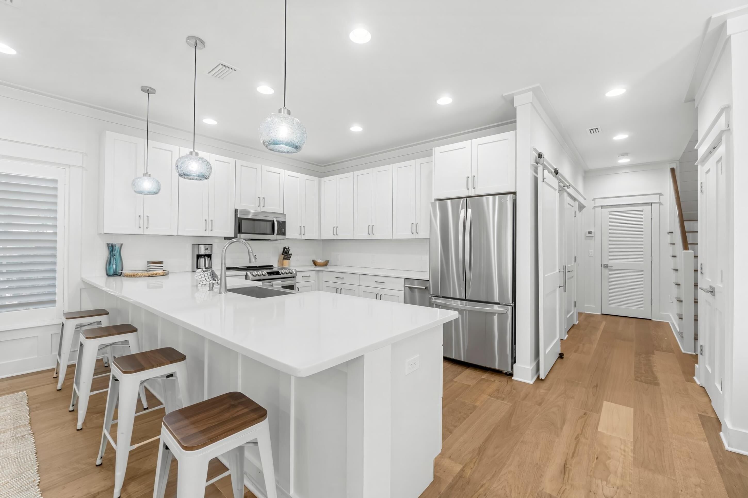 A modern kitchen with white cabinetry, stainless steel appliances, and a central island with bar stools.