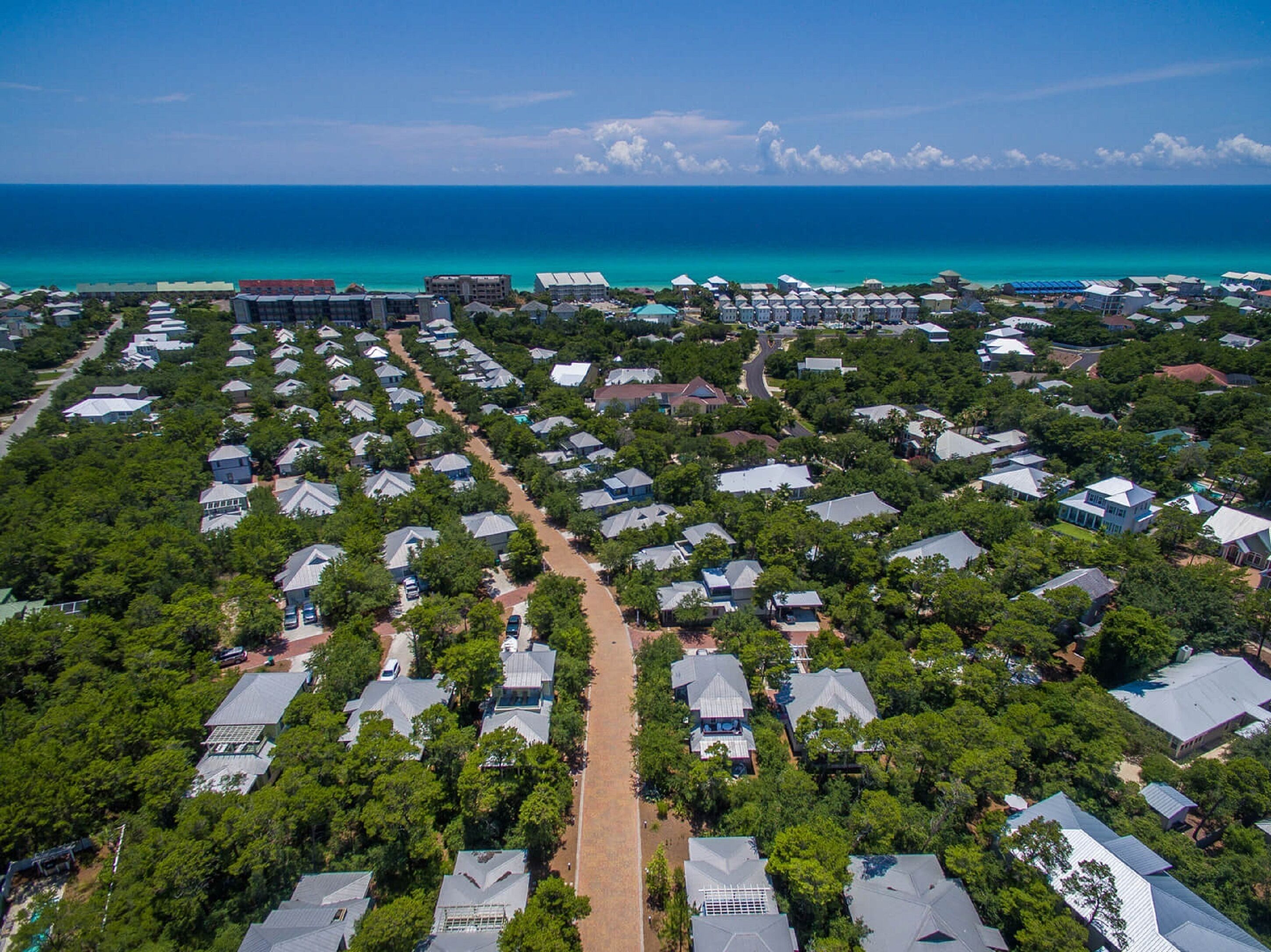 Una vista aerea di una zona residenziale con case disposte a file, una strada centrale e vista sull'oceano.