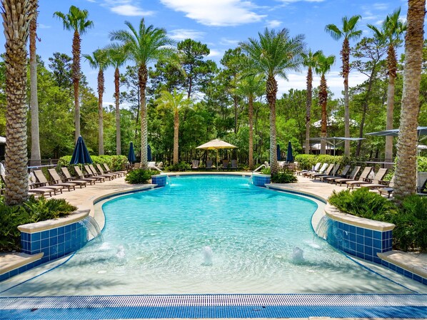 A swimming pool with lounge chairs and umbrellas, surrounded by palm trees. - Magnolia Cottages by the Sea by Panhandle Getaways (Panama City Beach)