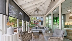 Ein überdachter Balkon mit Korbmöbeln, einem Deckenventilator und Blick auf das Haus.