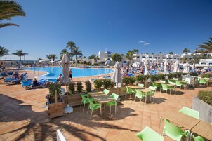 A poolside area with lounge chairs and umbrellas, a pool, and a dining area with tables and chairs.