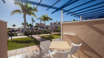 A patio with white chairs and a table, overlooking a pool and palm trees.