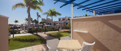 A patio with white chairs and a table, overlooking a pool and palm trees.