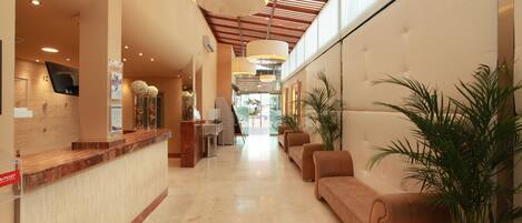 A hotel lobby with a reception desk, seating area, and a large window.