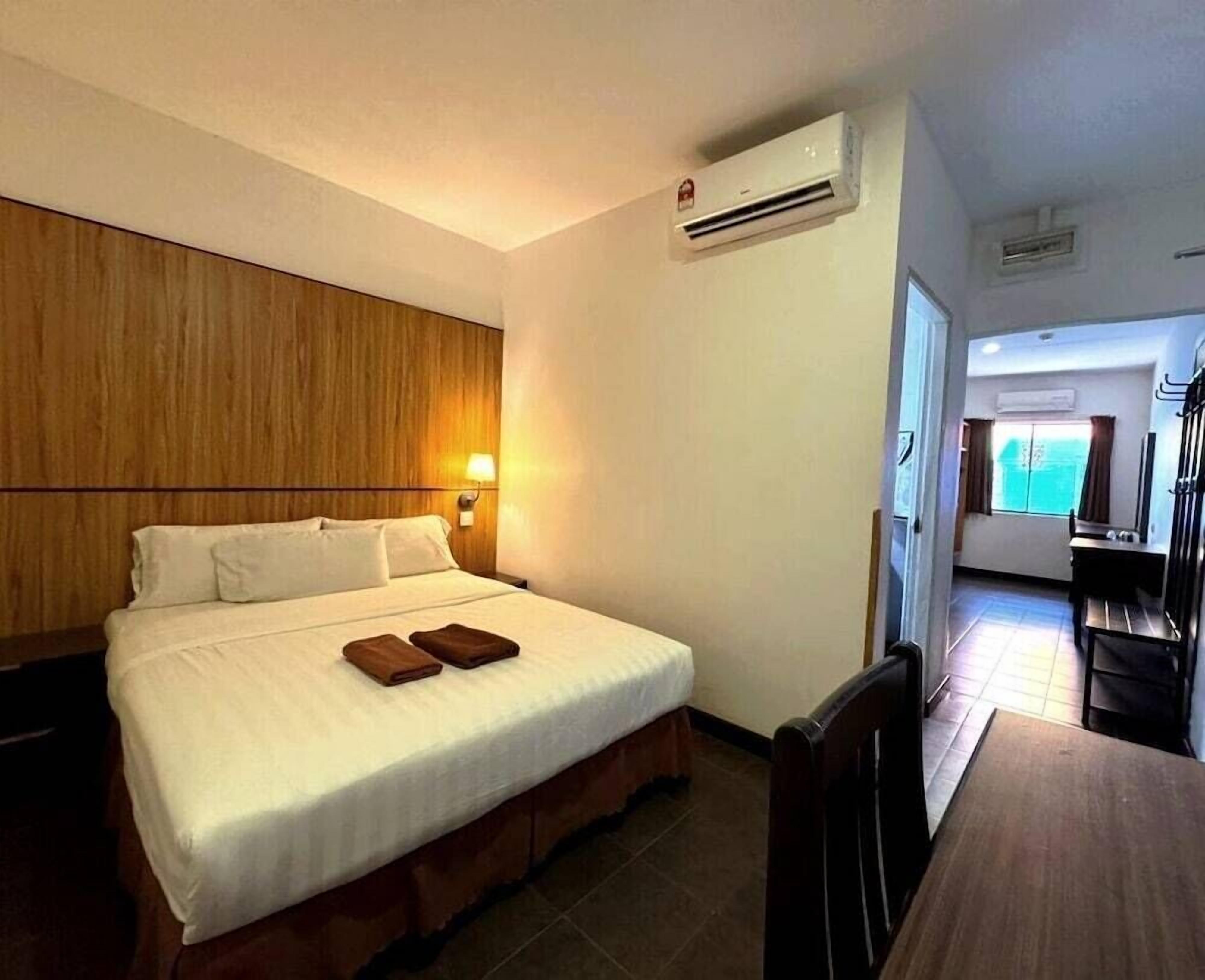 A hotel room with a bed, bedside table, lamp, and an air conditioning unit.