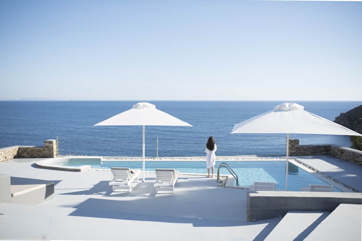 Zona junto a la piscina con vista al mar, sillones de playa y sombrillas.