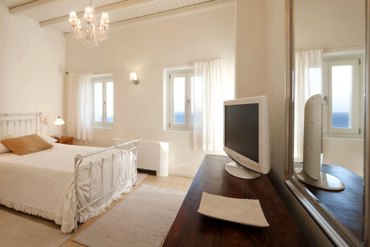 Un dormitorio con cama, mesitas de noche, televisor y un espejo grande.