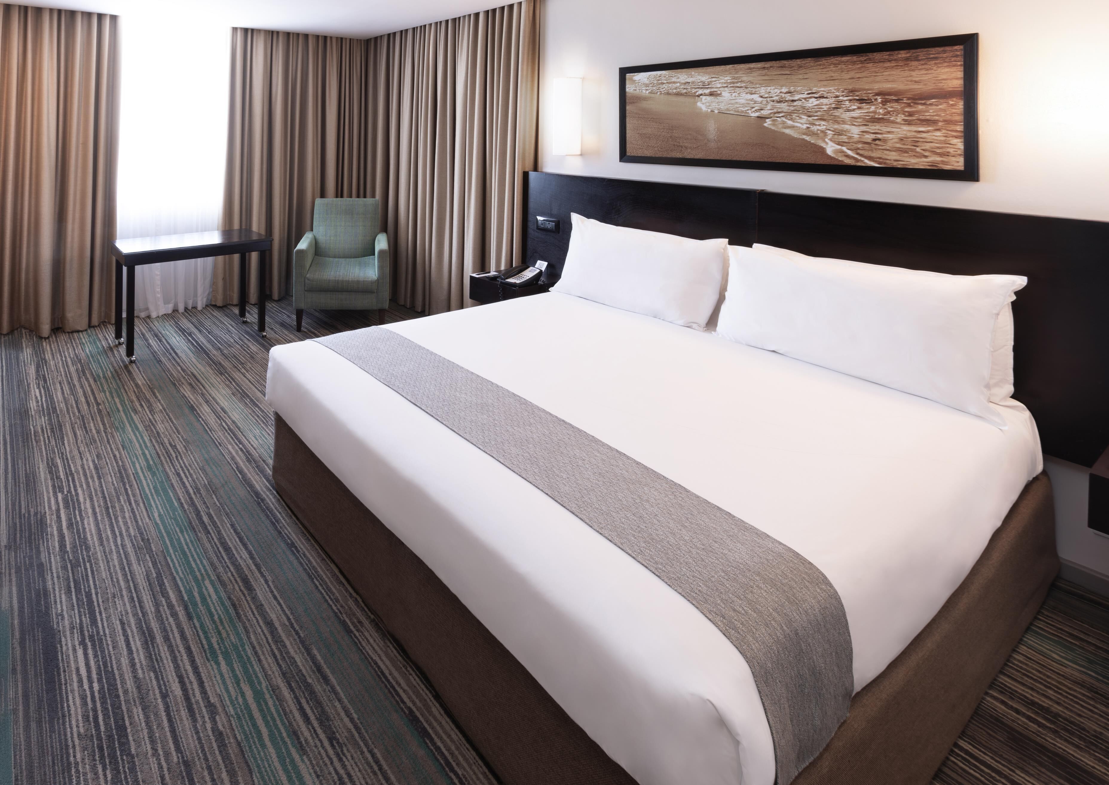 A hotel room with a large bed, a desk, a chair, and a painting on the wall.