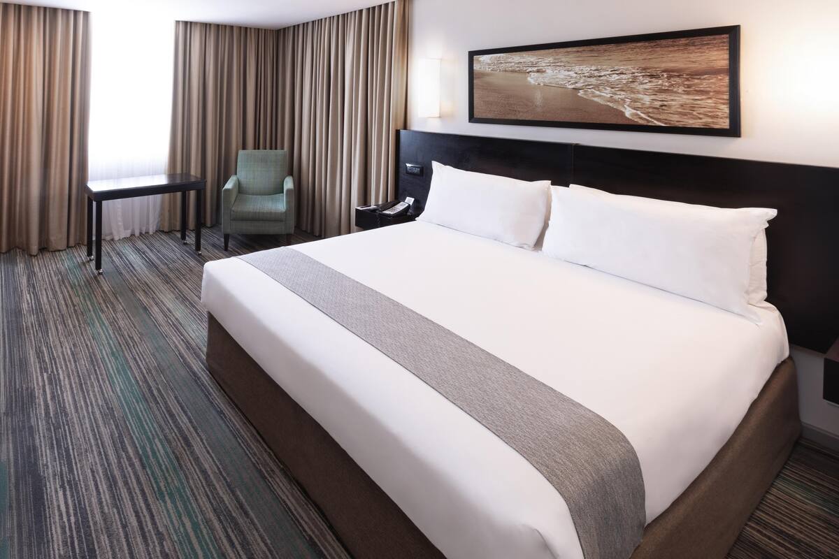 Une chambre d’hôtel avec un grand lit, un bureau, une chaise et un tableau au mur.