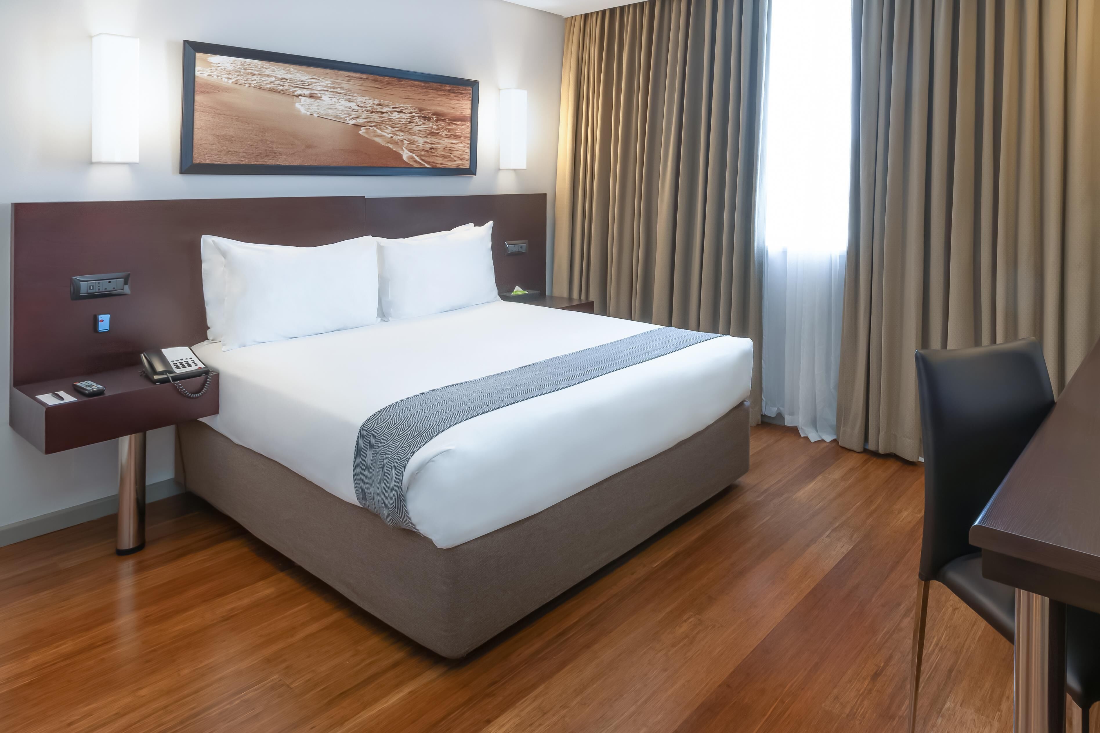 A hotel room with a large bed, a desk, and a chair.