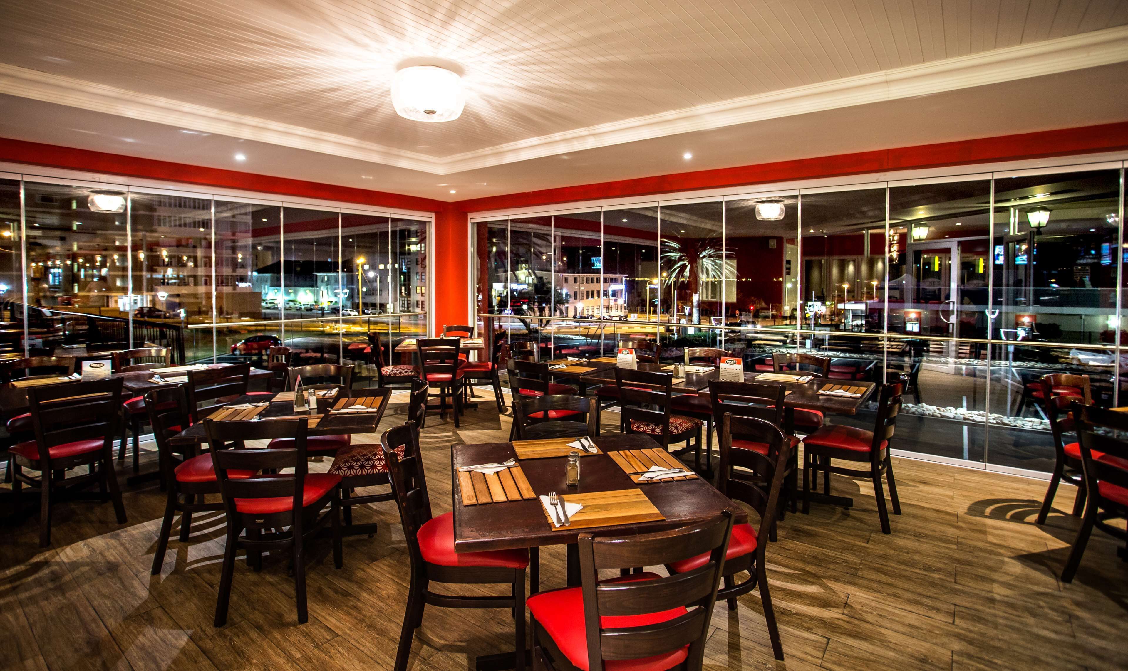 A restaurant with multiple tables and chairs, large windows, and a view of the city at night.