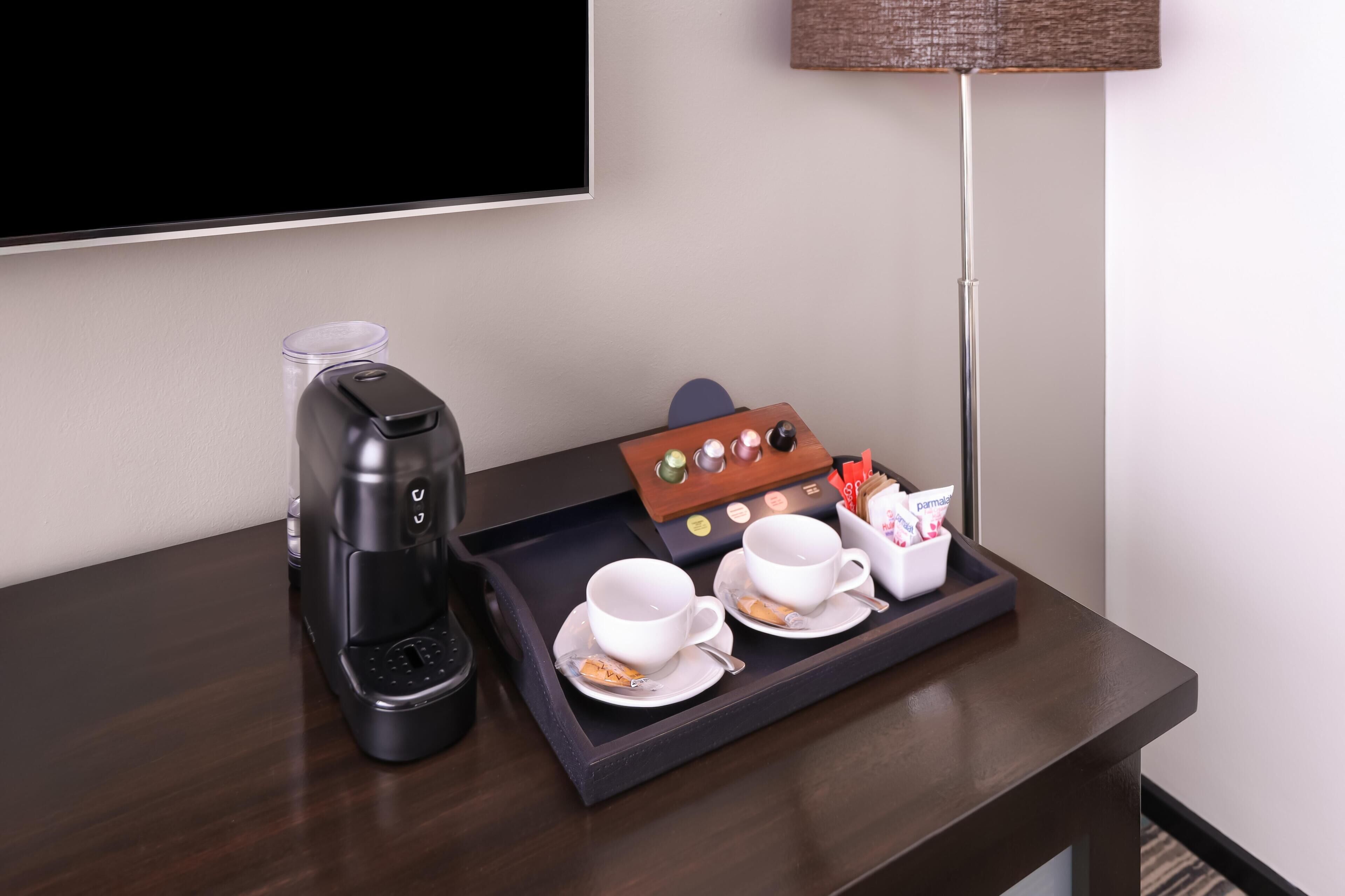 Habitación de hotel con cafetera, una bandeja con dos tazas y una caja de bombones.