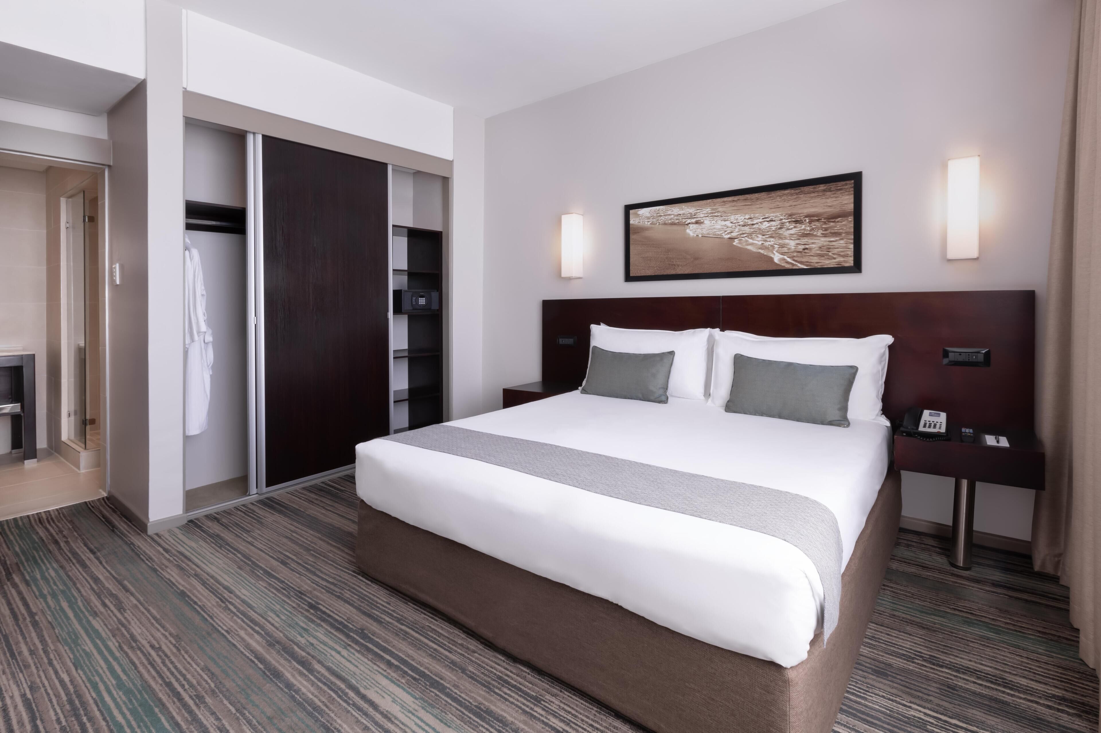 Habitación de hotel con una cama grande, un armario, una mesita de noche con teléfono y un cuadro en la pared.