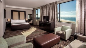 A hotel room with a large bed, a desk, a TV, and a view of the beach. - Garden Court Kings Beach (Gqeberha (Port Elizabeth))