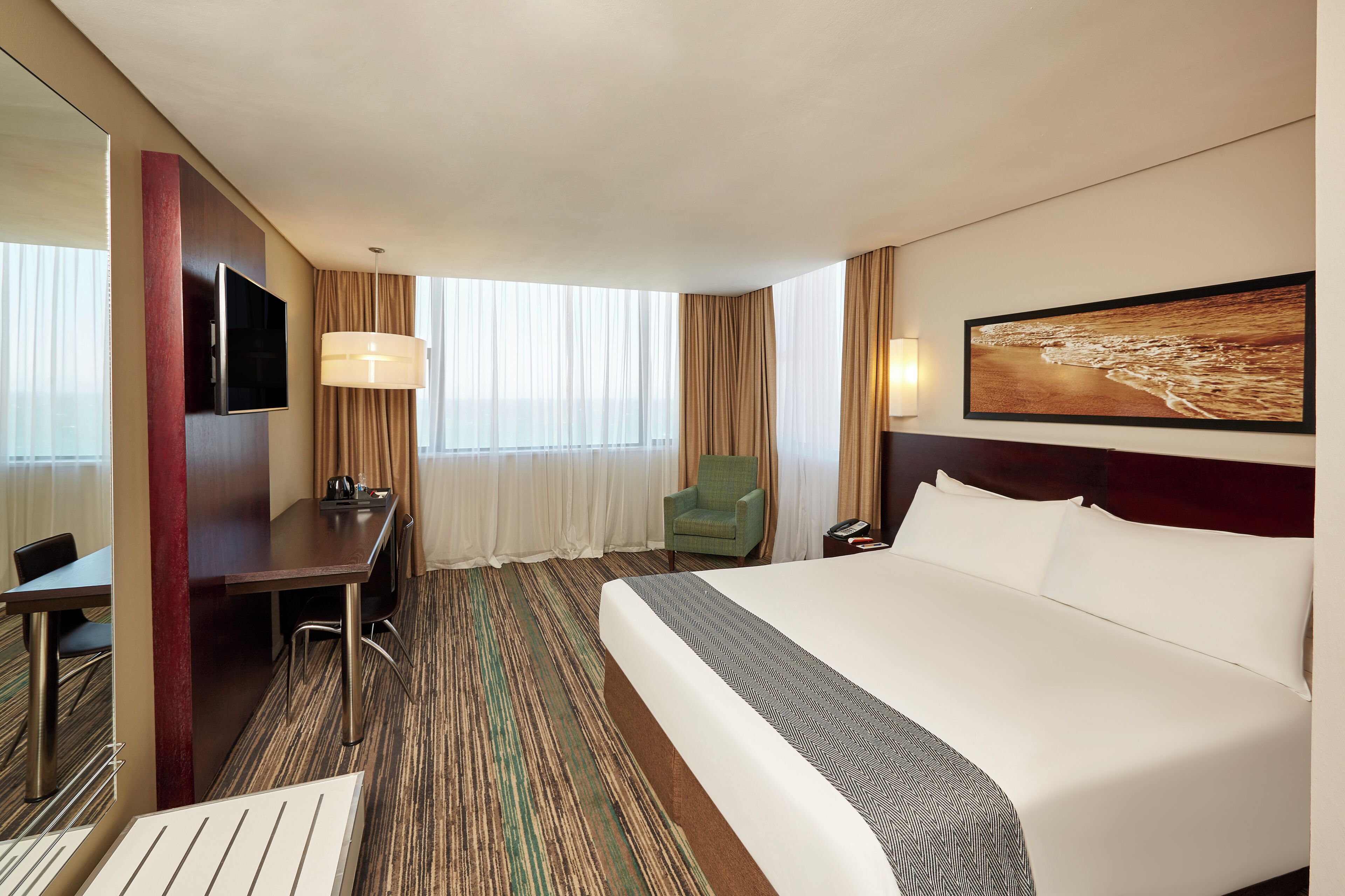 Ein Hotelzimmer mit einem großen Bett, einem Schreibtisch, einem Stuhl, einem Fernseher und einem fensterbepflanzten Fenster.