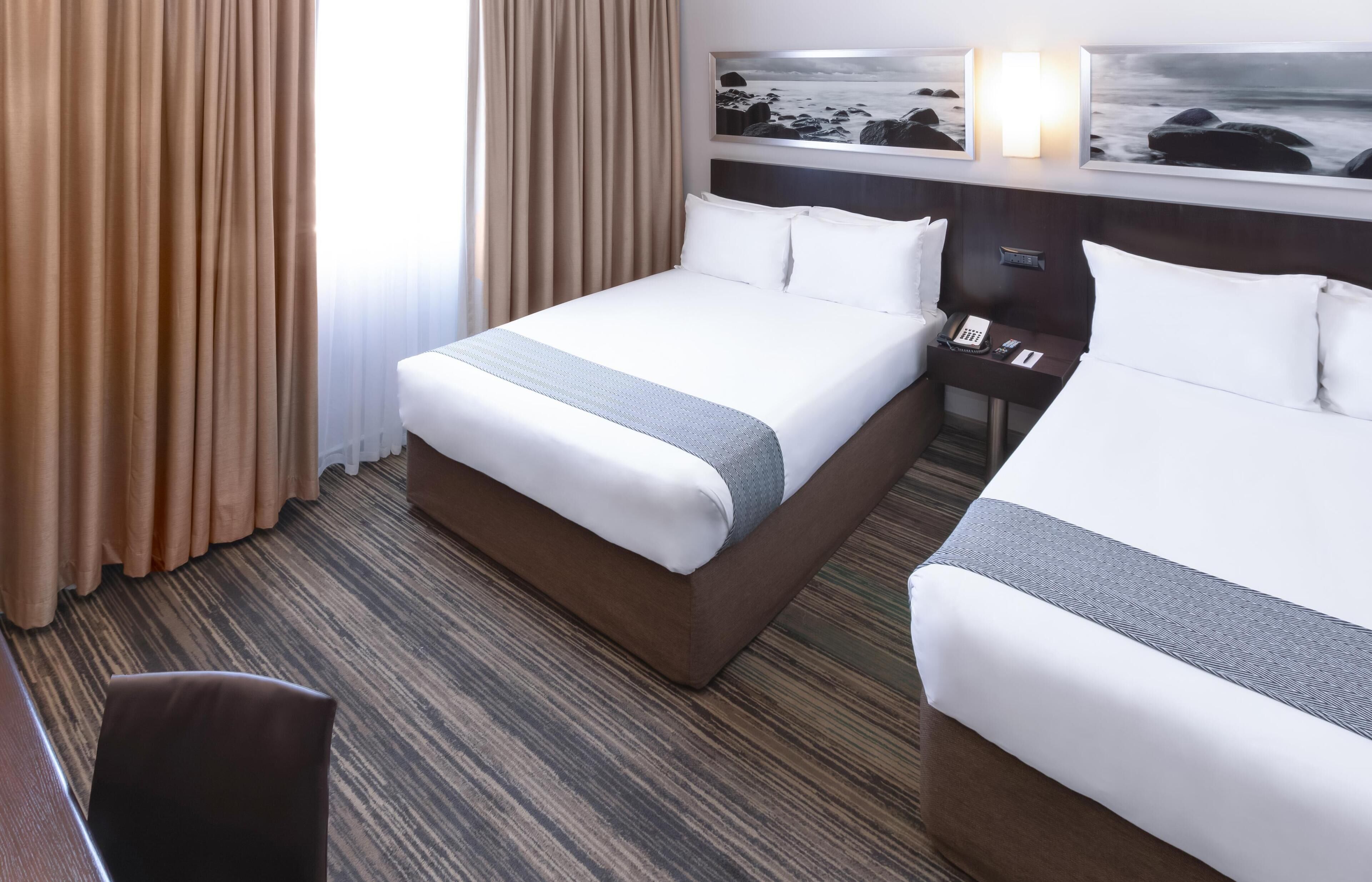 A hotel room with two beds, a desk, and a view of the ocean through a window.