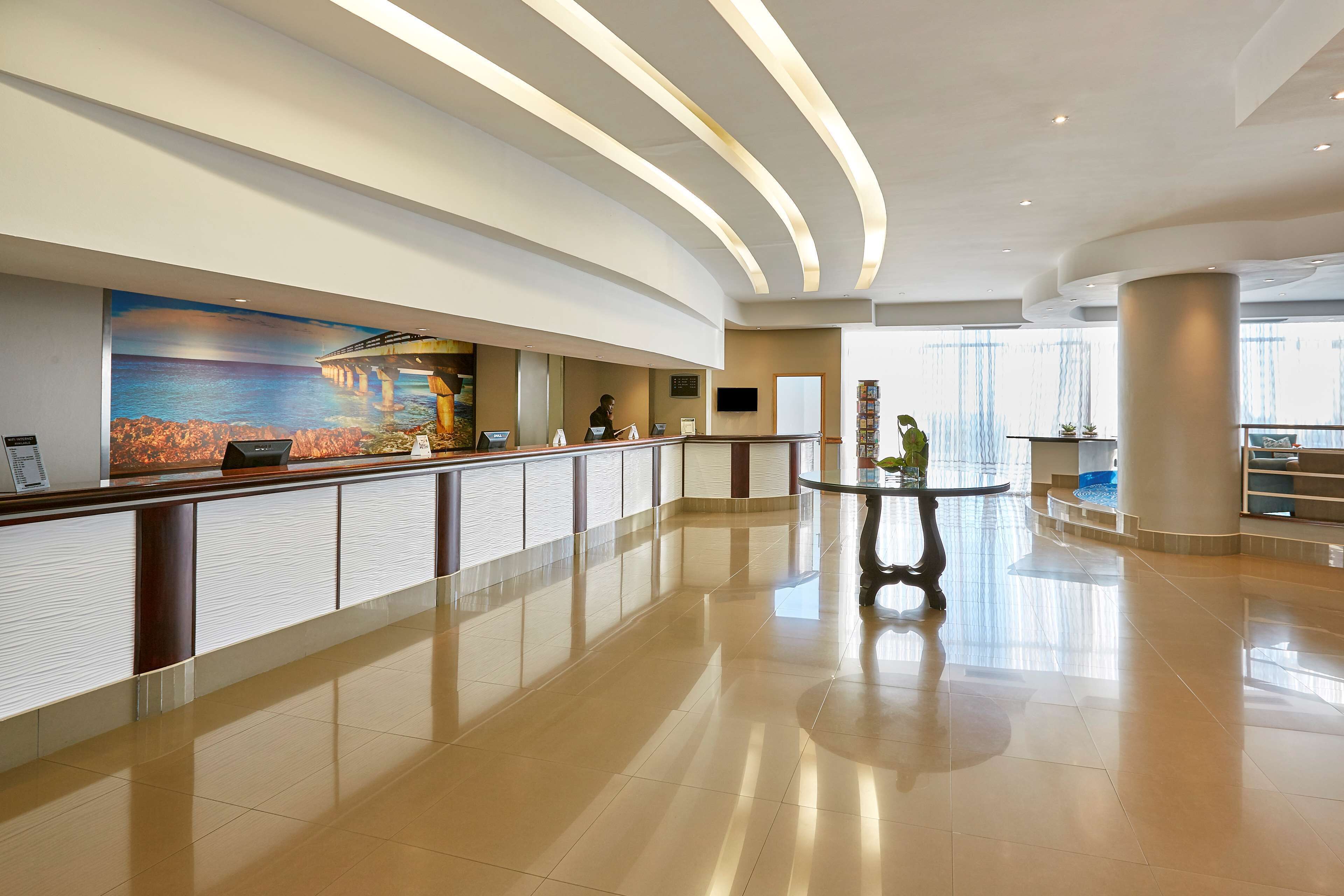 A spacious lobby with a reception desk, a large mural, and a modern staircase.