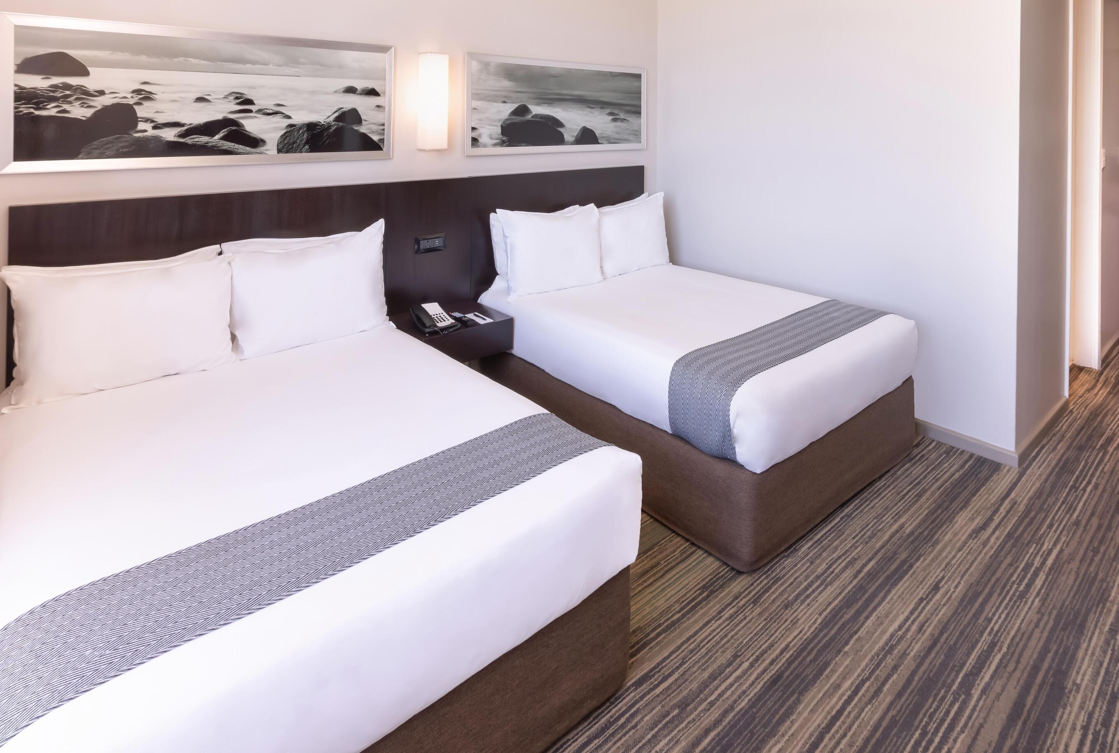 Una habitación de hotel con dos camas, una mesita de noche con teléfono y una obra de arte en la pared.