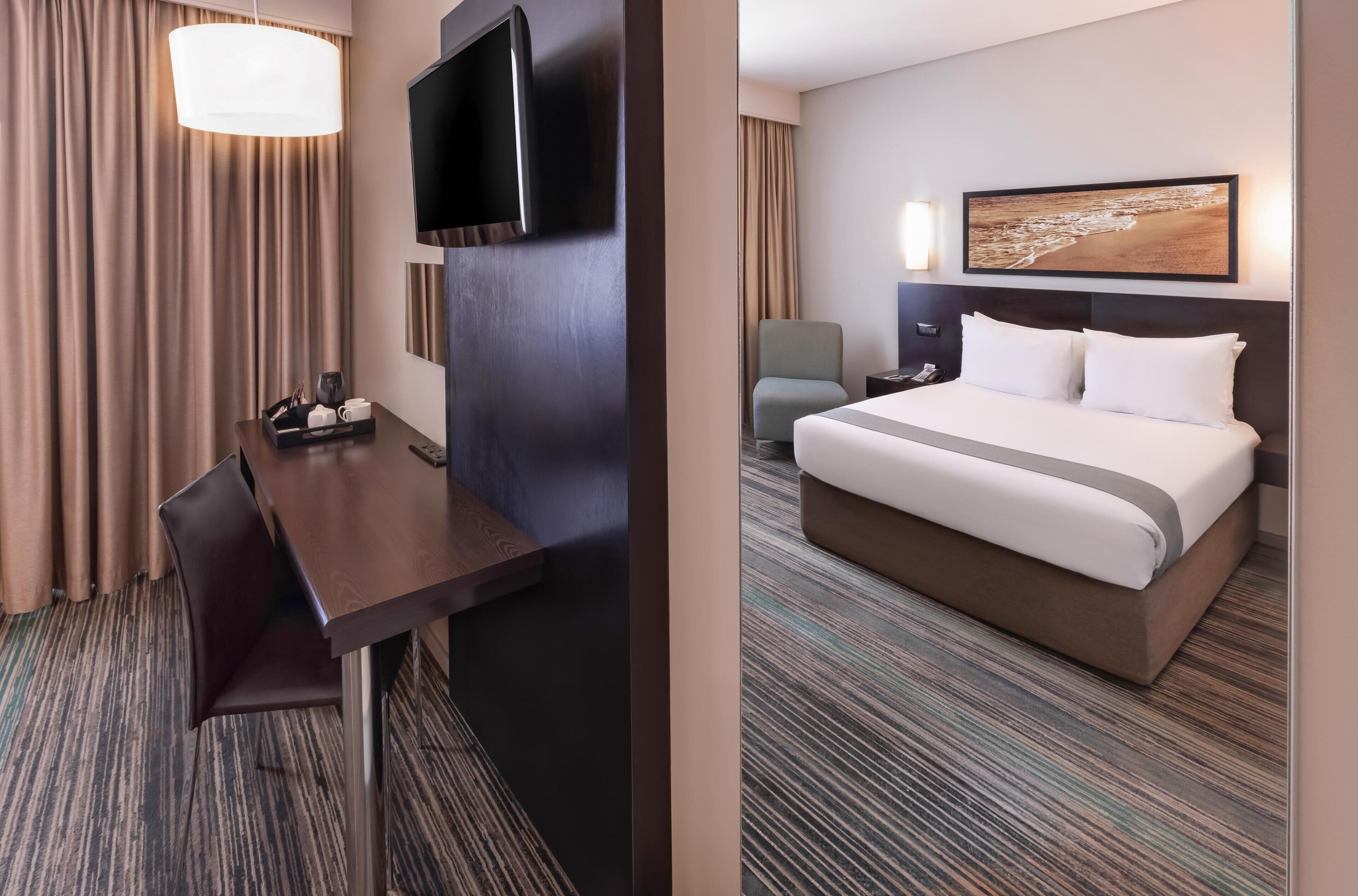 Habitación de hotel con cama, escritorio, silla, televisor y un cuadro en la pared.