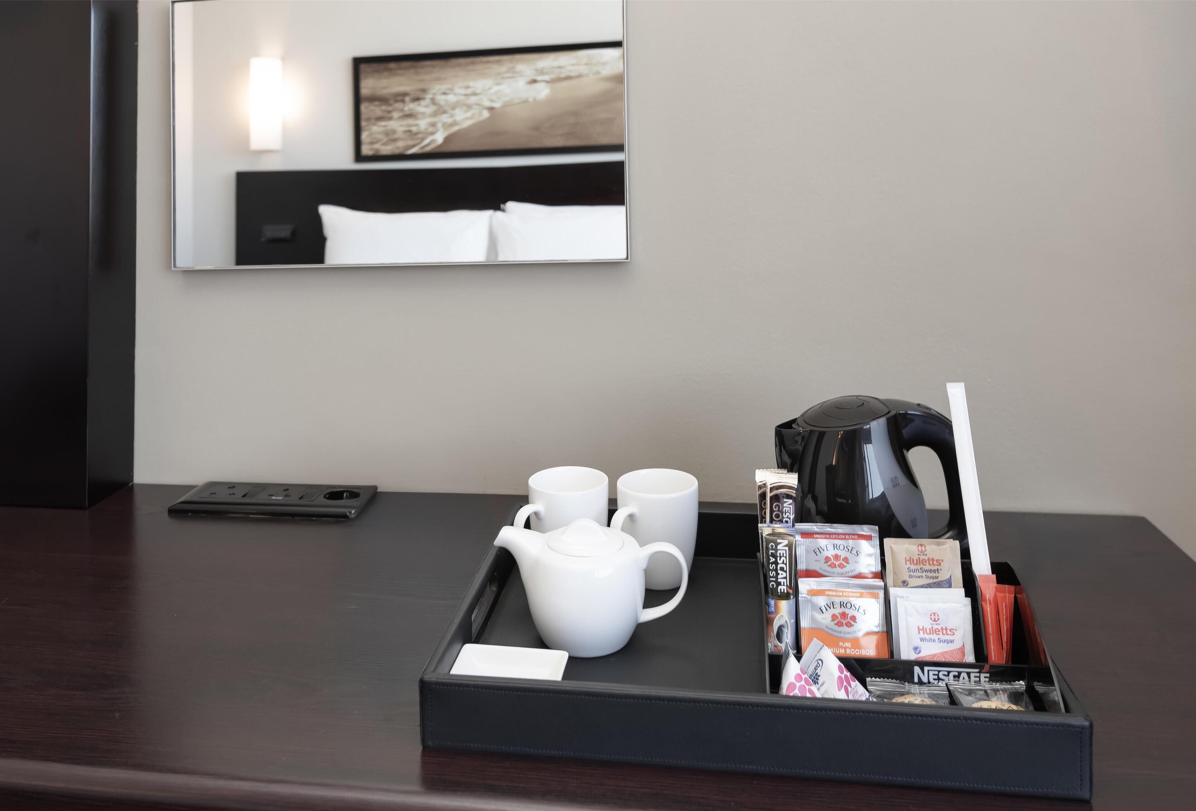A hotel room with a tray containing a teapot, two cups, and a kettle.
