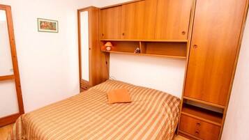 Quarto com cama, guarda-roupa de madeira e uma pequena prateleira.