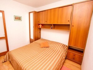 Un dormitorio con cama, armario de madera y una pequeña estantería.