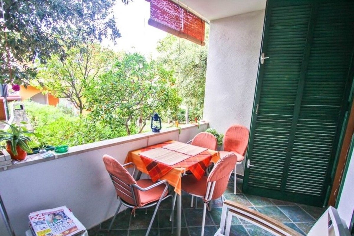 A balcony with a table and chairs, a small stool with a magazine, and a green door.