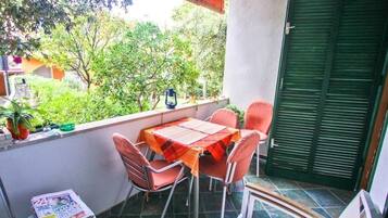 Un balcone con tavolo e sedie, un piccolo sgabello con una rivista, e una porta verde.