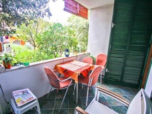 Un balcón con una mesa y sillas, un taburete pequeño con una revista, y una puerta verde.