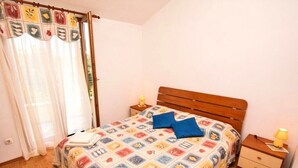 A bedroom with a wooden bed, a nightstand, a lamp, and a checkered rug. - Apartments Irena (Zadar)