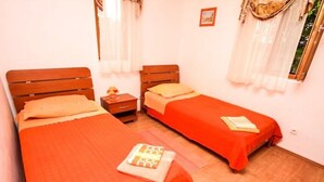 A room with two beds, each with a wooden headboard and orange bedding. There are nightstands with lamps and a small table with a book. - Apartments Irena (Zadar)
