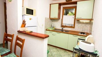 Una cucina compatta con mobili verdi, un forno a microonde, un tostapane e una piccola finestra con tenda.