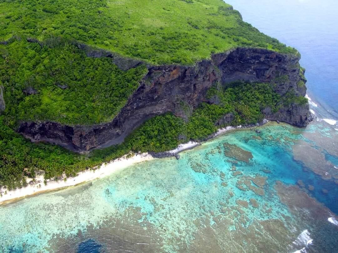 Paisagem costeira com penhasco, praia e águas verde-turquesa.