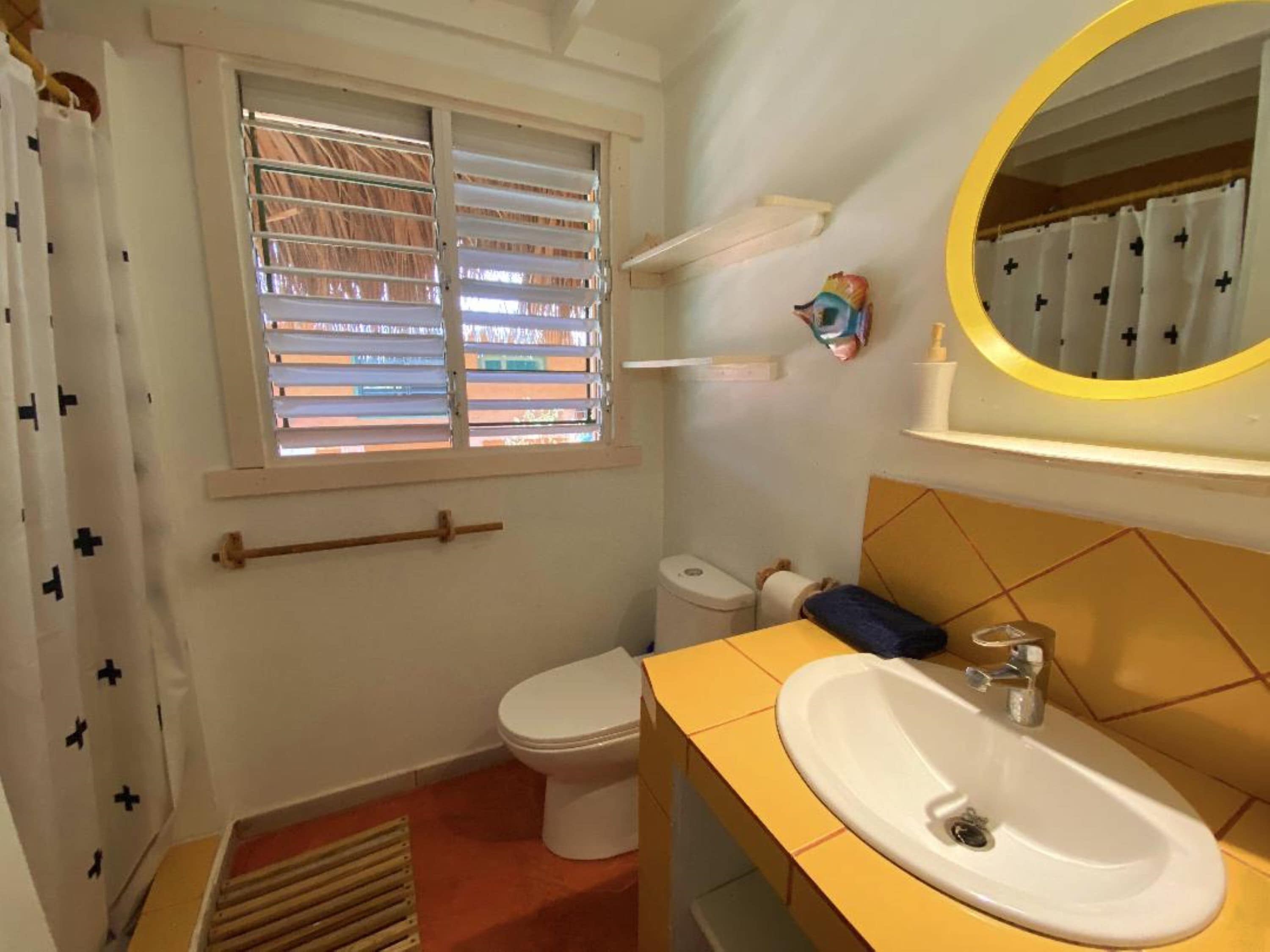Een kleine badkamer met toilet, wastafel en raam met zonwering.
