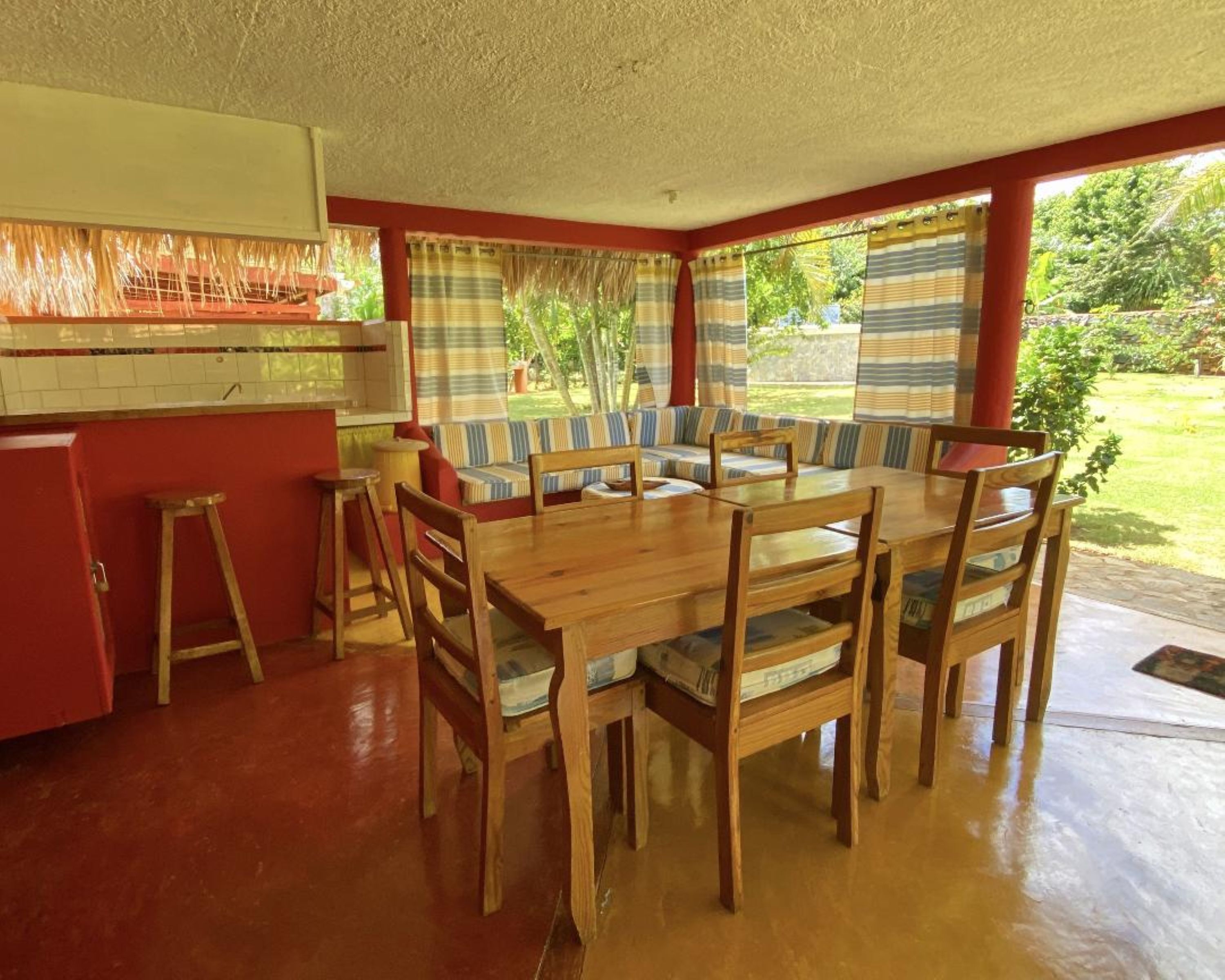 Een eetgedeelte met een houten tafel en stoelen, een gestreept sofa, en een keuken met een rode kast.