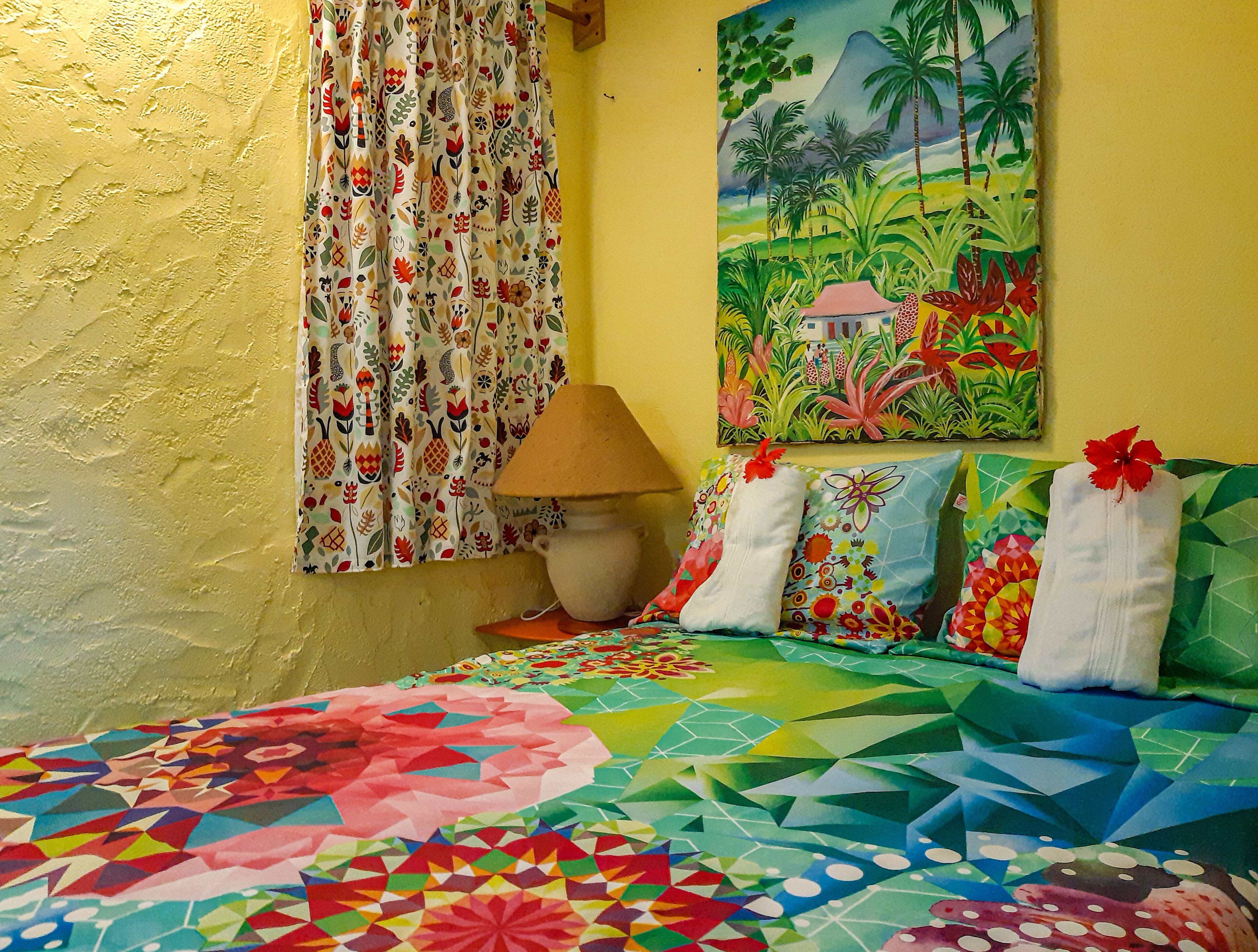 A room with a bed, colorful curtains, a painting, and a lamp.