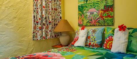 A room with a bed, colorful curtains, a painting, and a lamp.
