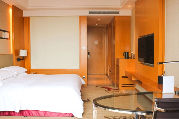 Una habitación de hotel con una cama, televisión, una mesita de vidrio y un escritorio.