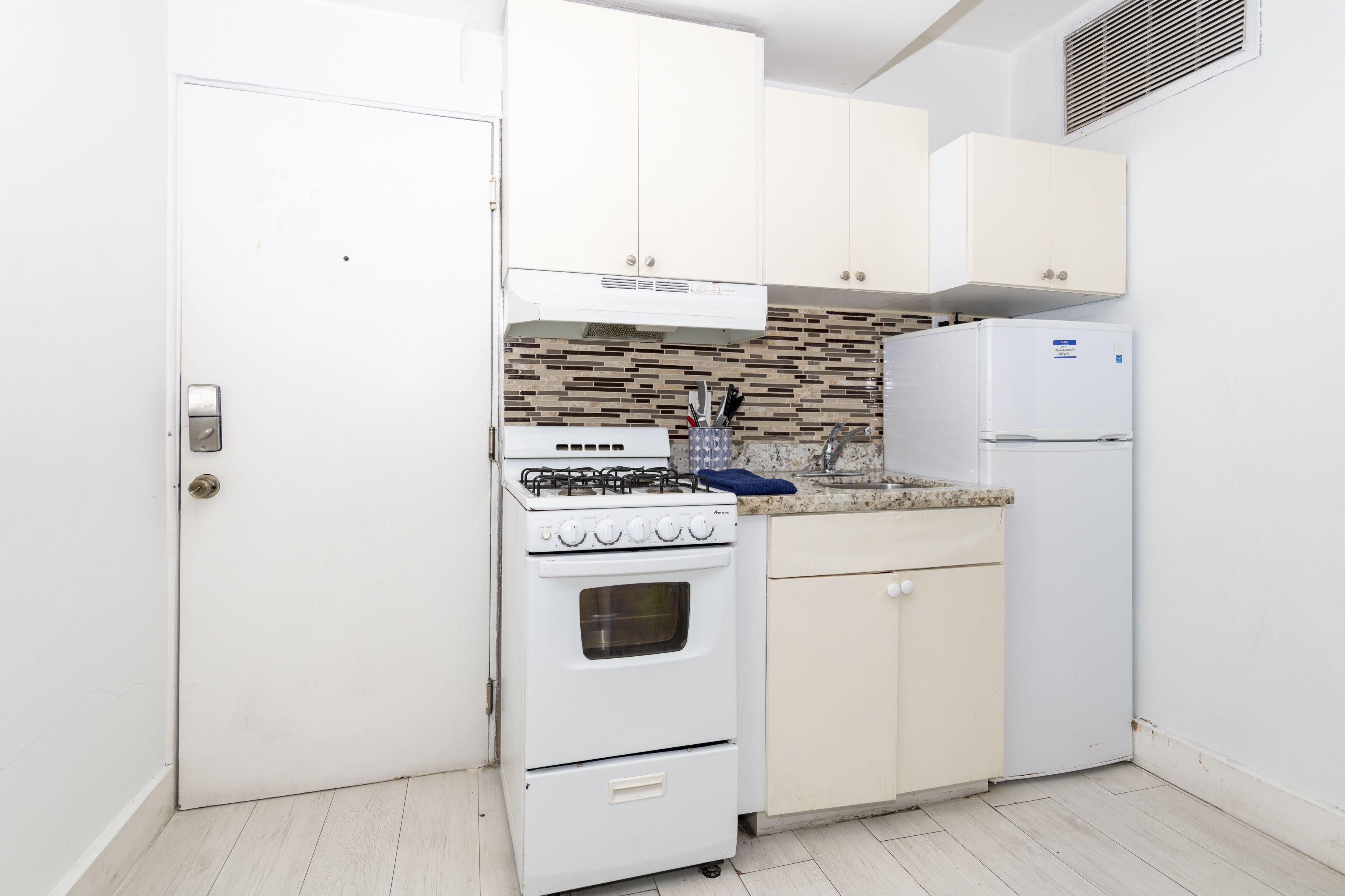 A compact kitchen with white cabinetry, a gas stove, a built-in oven, a refrigerator, and a tiled backsplash.