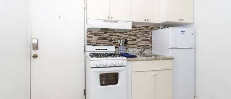 A compact kitchen with white cabinetry, a gas stove, a built-in oven, a refrigerator, and a tiled backsplash.