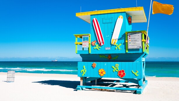 A lifeguard tower with a flag, a surfboard, and a beach warning sign. - 335 Ocean Walk Apartments (Miami Beach)