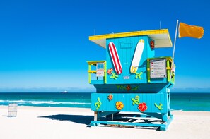 A lifeguard tower with a flag, a surfboard, and a beach warning sign.