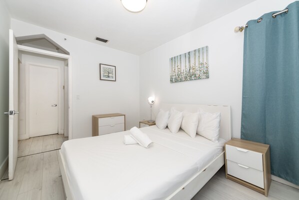 A bedroom with a bed, bedside tables, a nightstand, a wall-mounted lamp, and a door.
