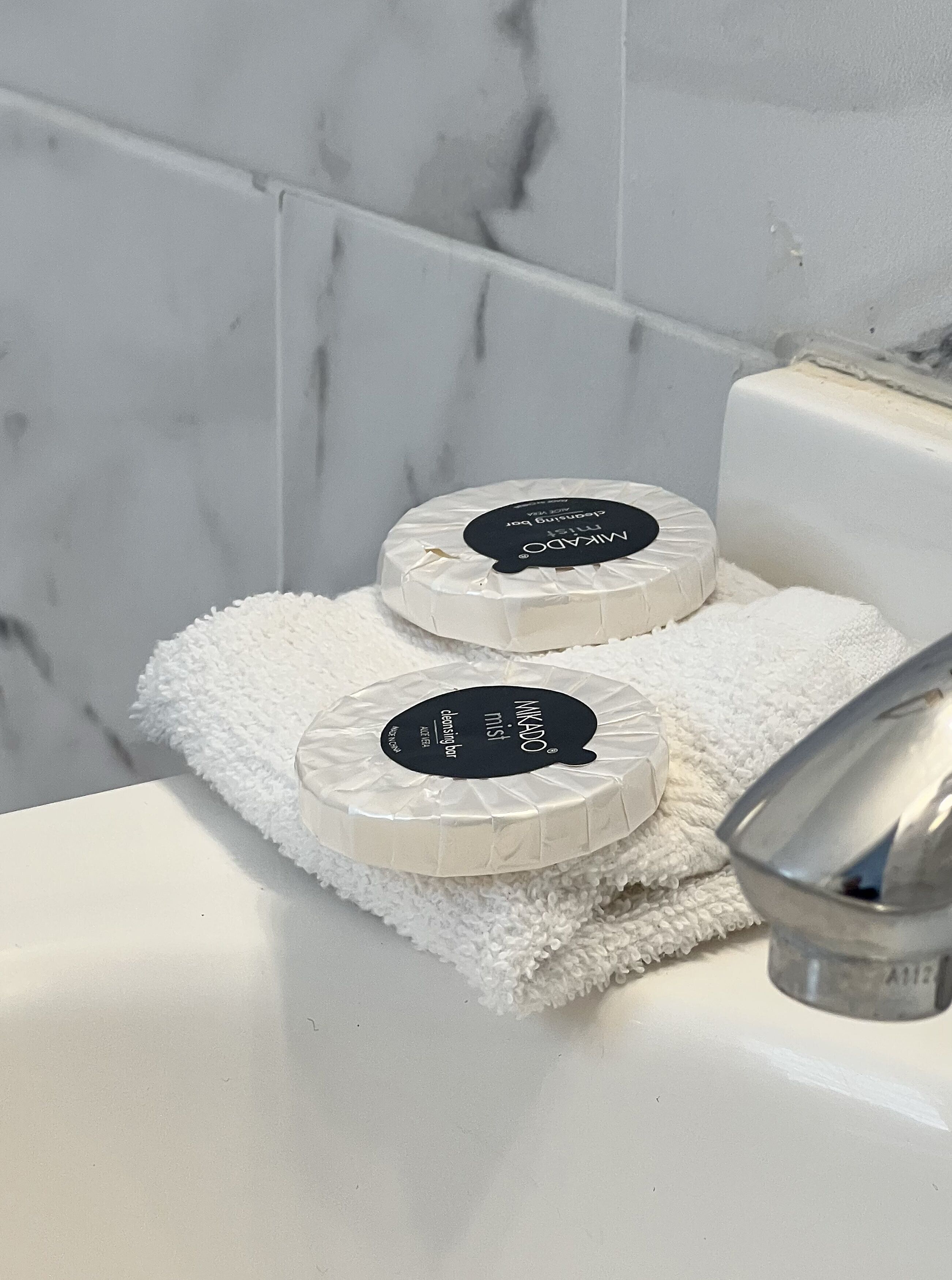 Two white, round, white fluffy bathmats with black labels on a white bathroom sink.