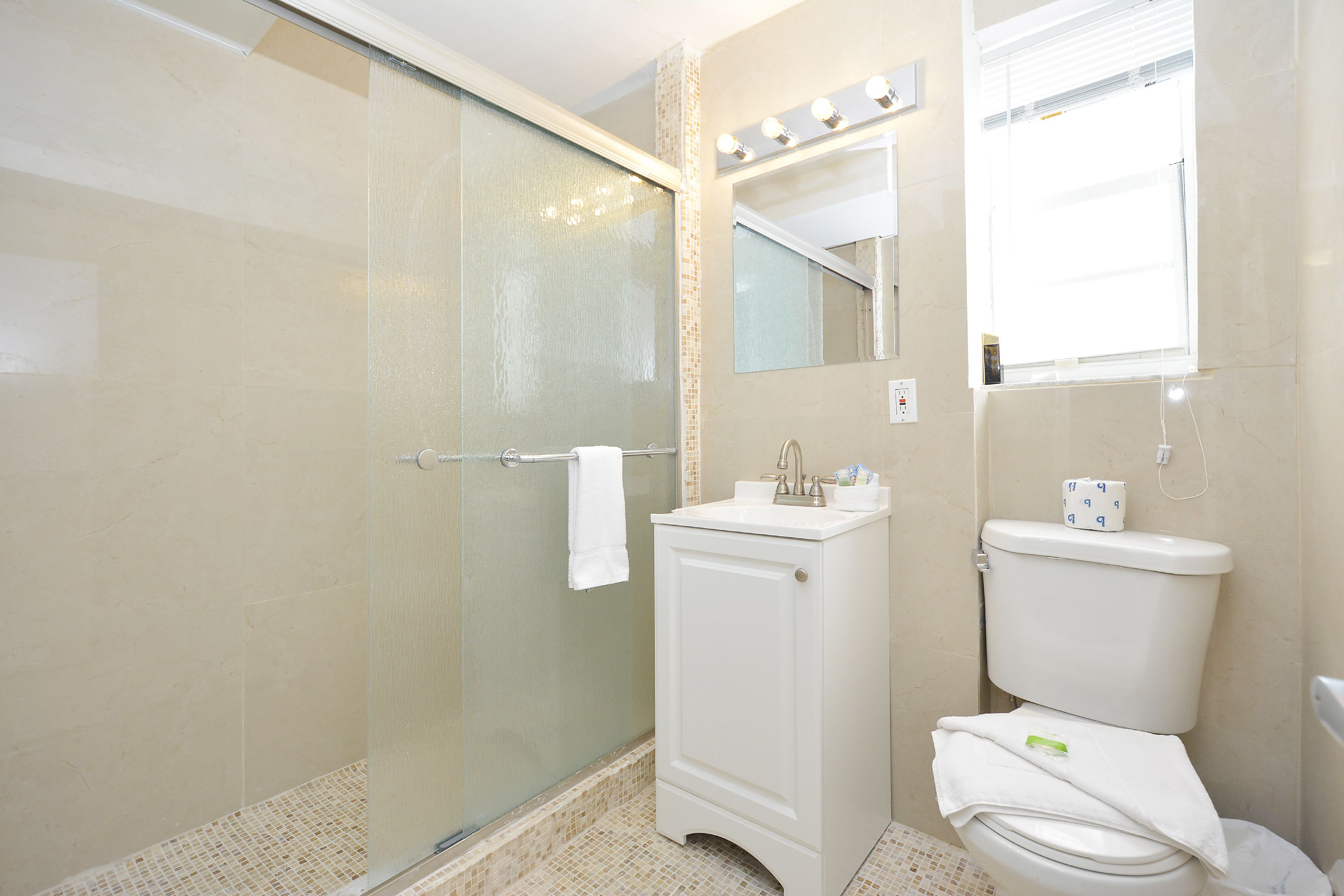 A bathroom with a glass shower enclosure, a white sink, and a toilet.