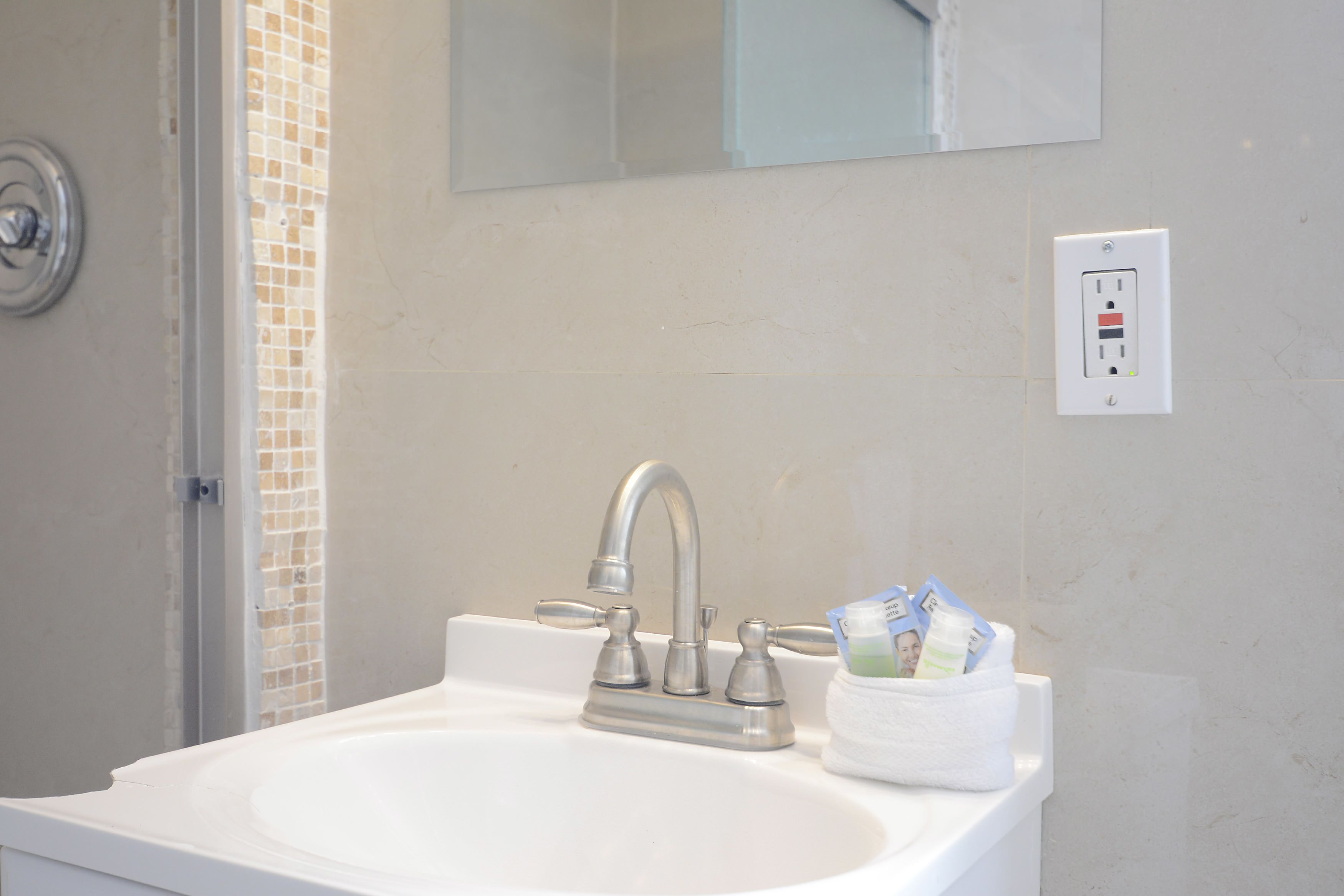 A bathroom sink with a modern faucet, a towel rack with a white towel, and a power outlet on the wall.