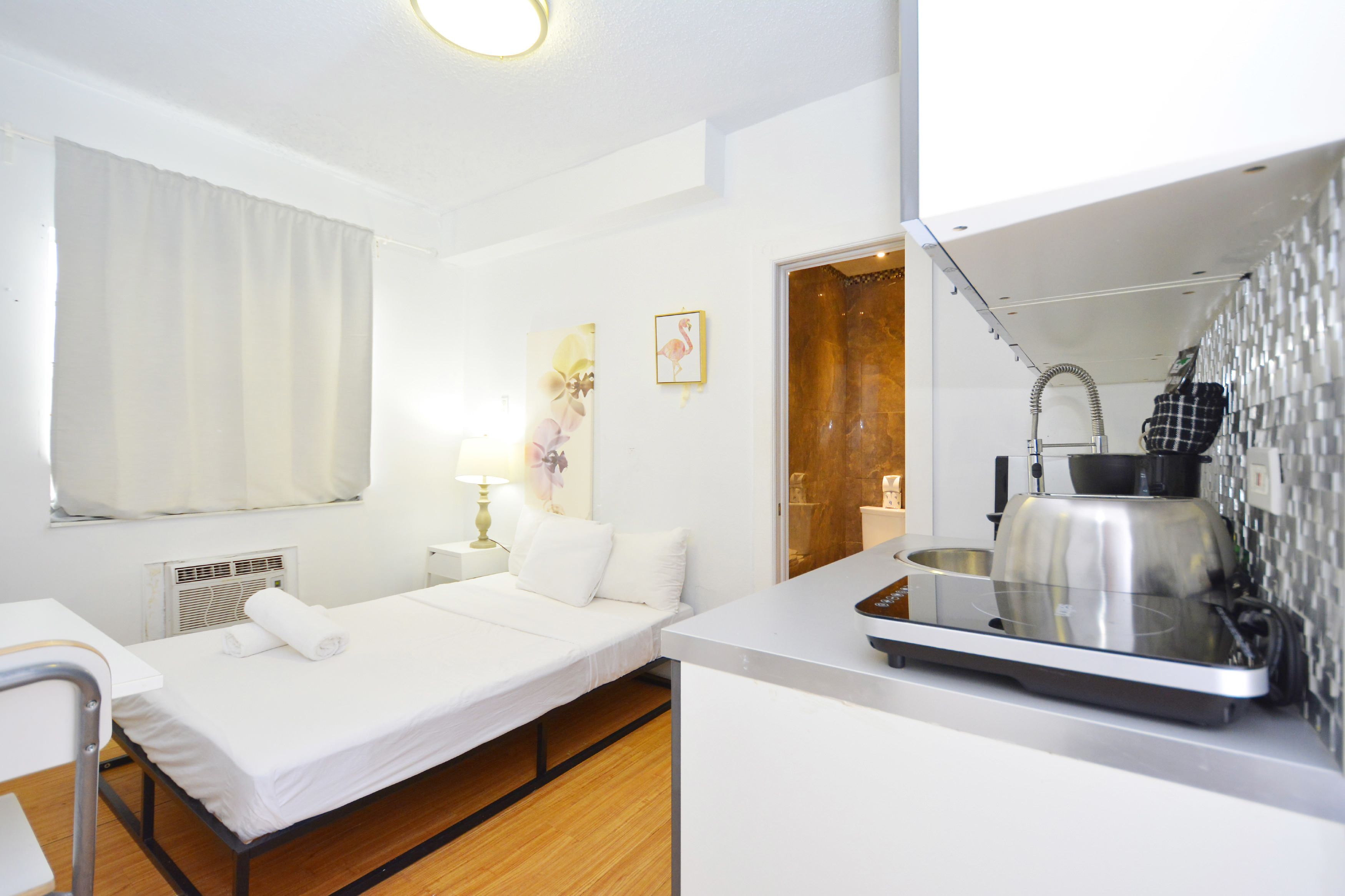 Une chambre d’hôtel de taille réduite, comprenant un lit simple, un petit bureau, une kitchenette et une salle de bain.