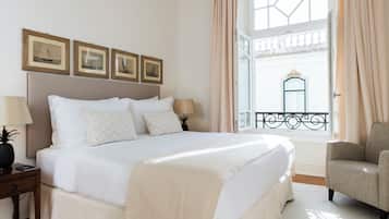 Un lit bien fait, avec une tête de lit, deux tables de chevet avec des lampes, et une vue sur un balcon doté d’une balustrade.