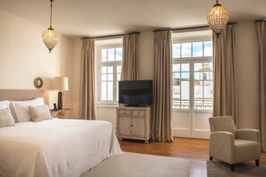 A hotel room with a large bed, a television, a chair, and a view of the city through large windows. - Bordoy Grand House Algarve (Vila Real Santo Antonio)